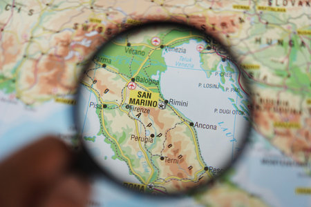 A woman's hand holding a magnifying glass looking at San Marino on a geographical mapの写真素材