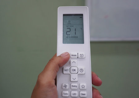 Close-up image of a hand holding a white AC (Air Conditioner) remote control to set the temperature...