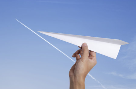 hand throwing a paper plane with jet-steam track on a clear blue sky 