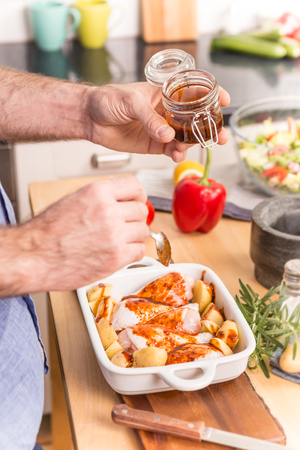 Man's or chef's hands preparing dinner (chicken drumsticks with potatoes) in a roasting dish - close up.の写真素材