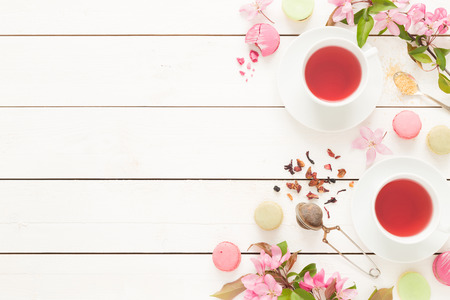 Pink fruity tea and pastel french macarons cakes on rustic white wooden background. Dessert in a garden. Flat lay composition (from above, top view). Free text space.の写真素材