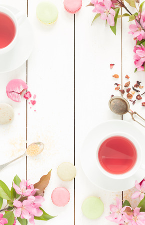 Pink fruity tea and pastel french macarons cakes on rustic white wooden background. Dessert in a garden. Flat lay composition (from above, top view). Free text space.