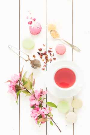 Pink fruity tea and pastel french macarons cakes on rustic white wooden background. Dessert in a garden. Flat lay composition (from above, top view).の写真素材