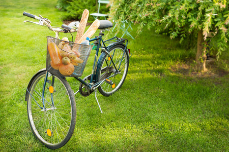 Bicycle with food products (groceries) in the basket. Green summer garden as background. Countryside lifestyle concept.の写真素材