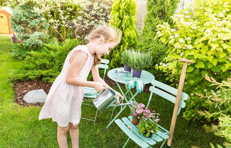 Eight years old blond caucasian child girl watering flowers outdoor in a summer garden.の写真素材