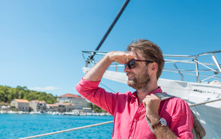 Forty years old caucasian tourist man or sailor in sunglasses standing by the sea marina with backpack. Yacht boat as background. Summer vacation (holiday), traveling and adventure.の写真素材