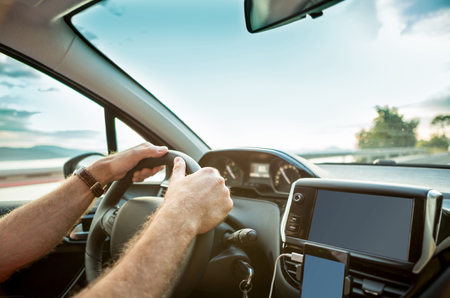 Man's (driver's) hands on steering wheel while driving a car - close up.の写真素材
