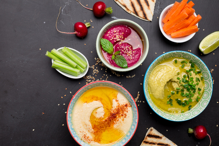 Colorful vegetarian snacks (appetizers) table. Various dips with pita bread. Black chalkboard as background. Flat lay composition from above (top view). Healthy diet or lifestyle concept.の写真素材