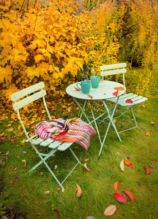Colorful autumn garden nook - pastel green table, cups of hot tea, chairs and blanket. Outdoor fall relaxation scenery - countryside lifestyle concept.の写真素材