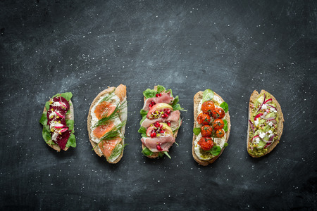 Different kinds of colorful sandwiches on black chalkboard background from above (top view). Party starter or appetizer - flat lay composition with free text space.の写真素材