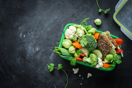 School lunch box with sandwich and various colorful vegetables on black chalkboard. Healthy eating habits concept. Flat lay composition (from above, top view). Background layout with free text space.の写真素材