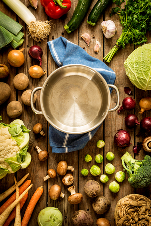 Cooking - empty pot with autumn (fall) vegetables around. Vintage rustic wood as background. Rural kitchen table - flat lay composition (from above, top view). の写真素材