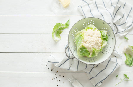 Fresh wet raw cauliflower in a strainer on rustic white wooden background. Preparing meal - rural kitchen scenery from above (flat lay, top view). Layout with free text space.の写真素材