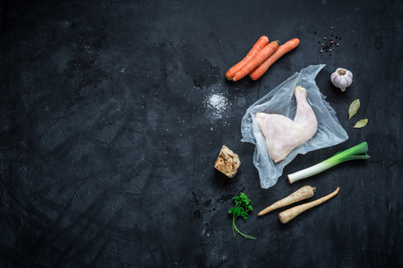 Cooking - chicken stock (bouillon, soup) recipe ingredients on black chalkboard background. Poultry and root vegetables - kitchen scenery from above (top view, flat lay). Layout with free text space.の写真素材