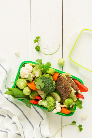 Green school or picnic lunch box with sandwich and various colorful vegetables. Healthy eating habits concept. Flat lay composition (top view) on white wood. Background layout with free text space.の写真素材