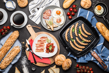 Full english breakfast on black chalkboard background captured from above (top view, flat lay). Coffee, fried eggs, baked beans, sausages, bread rolls, toast and bacon.の写真素材