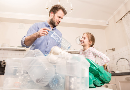 Recycling and ecology - happy caucasian family (father and daughter) sorting (segregating) household waste in the kitchen. Lifestyle - ecological education and awareness concept.の写真素材