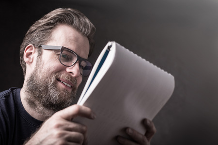 Happy smiling forty years old caucasian man (businessman) in casual t-shirt and glasses reading documents. Dark gray background - layout with free text (copy) space. の写真素材
