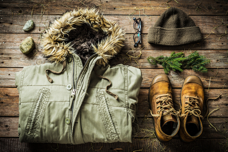 Warm male clothes (warm jacket, boots and hat). Winter or christmas weekend in country cottage (cabin) concept. Rustic cozy layout on wooden background captured from above (flat lay).の写真素材