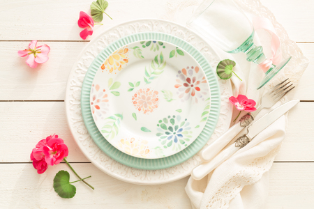 Easter, spring or summer table setting design captured from above (top view, flat lay). Ornamental plates, glass, cutlery and flowers. White wooden background. Outdoor garden party or picnic concept.の写真素材