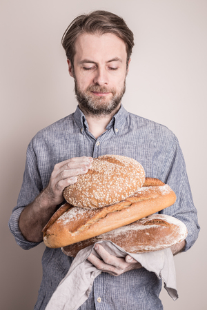 Baker man holding pile of rustic crusty loaves of bread. Small business and slow food concept.の写真素材