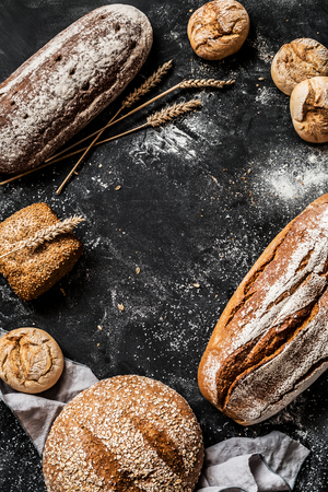 Bakery - gold rustic crusty loaves of bread and buns on black chalkboard background. Still life captured from above (top view, flat lay). Layout with free copy (text) space.の写真素材