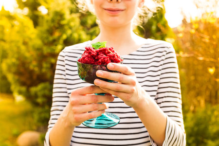 Raspberry sorbet in a young girl's hands outdoor. Garden party - summer cold, refreshing fruity...