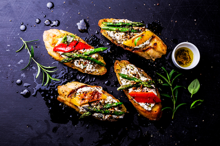 Colorful toasts (sandwiches) with cottage cheese, grilled pepper and asparagus on dark black background. Meal captured from above (top view, flat lay).の写真素材