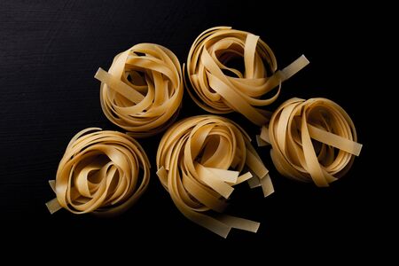 Raw tagliatelle pasta on black background close up. Captured from above (top view, flat lay). Dark moody composition.の写真素材