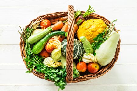 Colorful organic vegetables in wicker basket. Captured from above (top view) on white wooden background. Fresh harvest from the garden.の写真素材