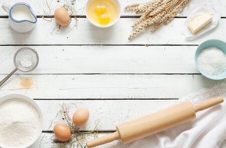Baking cake in rustic kitchen - dough recipe ingredients (eggs, flour, milk, butter, sugar) on white planked wooden table from above. Background layout with free text space.の写真素材