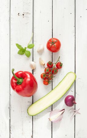 Mix of vegetables on white planked wood background - summer garden harvest. Red pepper, tomatoes, red onion, zucchini, garlic and basil from above. Ratatouille - french recipe ingredients.の写真素材