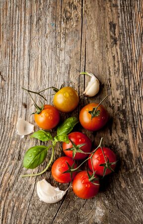 Cherry tomatoes, garlic and fresh basil on vintage wood table - rural still life from above. Harvest from garden. Background layout with free text space.の写真素材