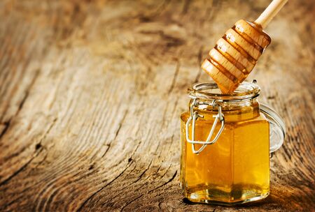 Honey dipper in a jar on an old vintage wood. Background layout with free text space.の写真素材