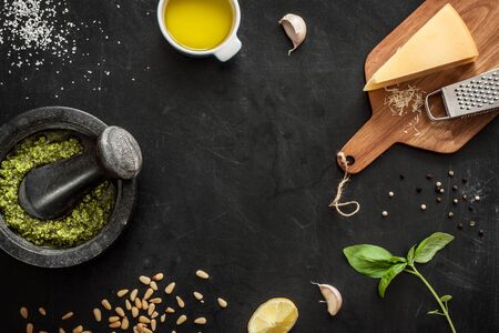 Green basil pesto - italian recipe ingredients on black chalkboard from above. Parmesan cheese, basil leaves, pine nuts, olive oil, garlic, salt, pepper and mortar. Layout with free text space.の写真素材