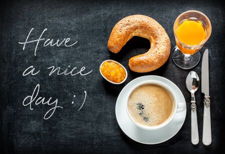 Have a nice day poster design with continental breakfast on black chalkboard background. Bar morning menu - coffee, orange juice, crescent roll and jam from above (top view, flat lay).の写真素材