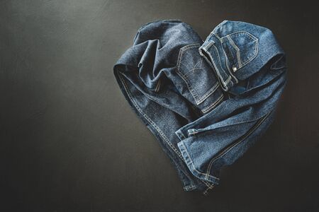 Clothing - heart shape made of two pairs of jeans. Denim trousers captured from above (top view, flat lay). Black chalkboard background with free copy (text) space.の写真素材