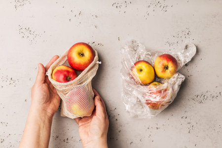 Eco friendly shopping concept. Hands holding apples in a zero waste mesh cotton bag versus fruits in...