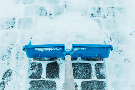 Cold snowy winter - blue shovel removing snow from the paver path (sidewalk) outdoor.の写真素材