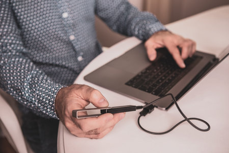 Man (businessman, investor) using laptop computer and cryptocurrency cold wallet at home.