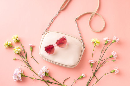 Fashion spring accessories for woman. Small white handbag (purse), heart shaped sunglasses and flowers on pastel pink background. Free copy (text) space.の写真素材
