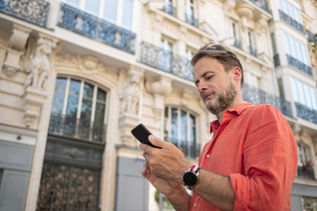 Caucasian man (businessman) using smartphone in the elegant street. Typical architecture of Parisian streets in the background.の写真素材