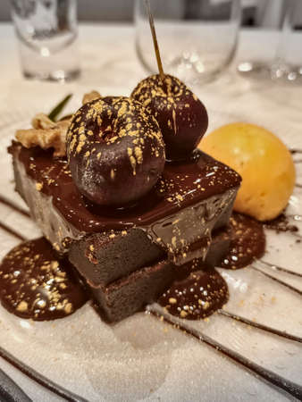 Rich chocolate brownie with orange ice cream and melted chocolate on top with golden decorationの写真素材