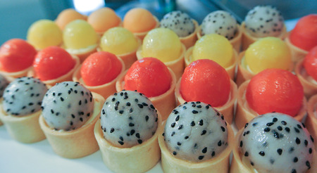 Rows of various kinds of fruits in round shape, put on cream on pastry cups, The front row is Pitahaya or dragon fruit, then water melon and yellow melon.の写真素材