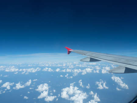 Airplane wing with red tip, against blue sky and white clouds.の写真素材