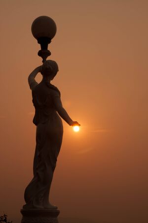 Statue of a women with her hand resting on the setting sun の写真素材