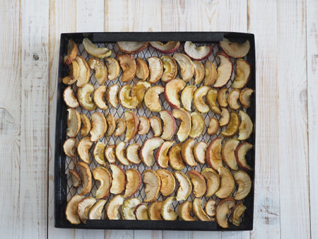 Sliced apples are dried on a metal wire rack from a home dryer. Wooden white rustic table.