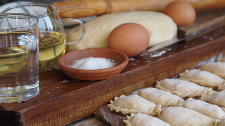Wooden background with dumplings and dough ingredients for making dumplings. Food and cooking...