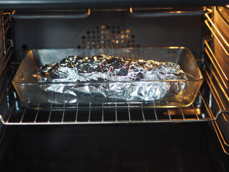 Food covered with foil on a glass baking sheet in a home kitchen oven is ready to cook.