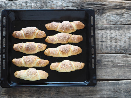 Croissants sprinkled with sesame and sugar on an oven tray on an ancient wooden background.Homemade...